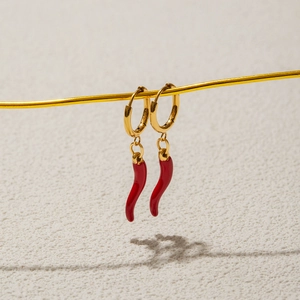 Elegant gold hoop earrings with red chili pepper pendants on a beige textured background