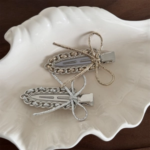 Detail of gold and silver metal chain bow hair clips on a white shell ceramic plate