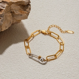 Detailed macro of a two-tone gold and silver paperclip chain bracelet on a textured rock