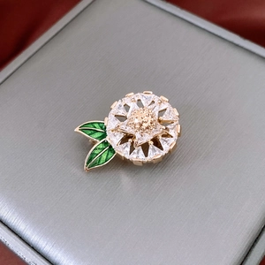 Detail of 14K gold plated flower brooch with green enamel leaves and white zircon