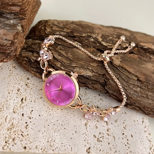 Close-up of rose gold bracelet watch with pink dial on natural wood and stone textures