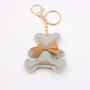 Close-up of beige faux leather bear keychain with brown bow and golden metal ring