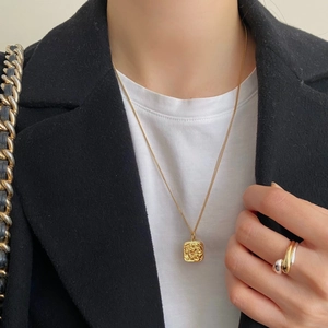 Detail of a gold square pendant necklace and two-tone ring on a professional model