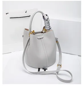 Detail of light gray lychee leather bucket bag with gold buckle and silk scarf handle