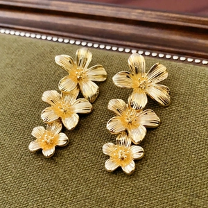 Detailed close-up of vintage gold floral earrings with triple tiered petals and brushed metal