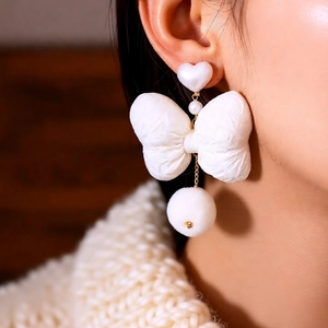 Detailed view of elegant white bow and fur pompom earrings on a model's ear