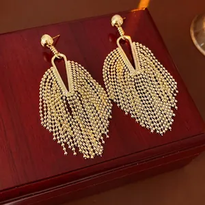 Elegant gold round stud earrings with long metal bead tassels on vintage wood background