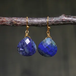 Detail of teardrop blue imperial stone earrings with gold wire wrap on a branch