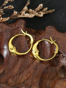 Macro shot of gold moon face earrings with crystal eyes on a rustic wood background