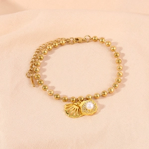 Detail of gold beaded bracelet with hollow shell charm and pearl shell pendant for women