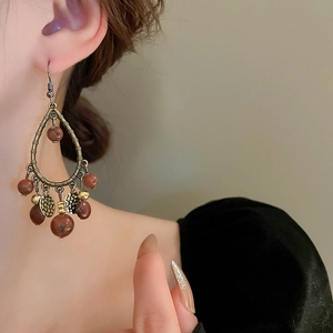 Detail of vintage bohemian drop earrings with reddish beads and metallic tassels on a model