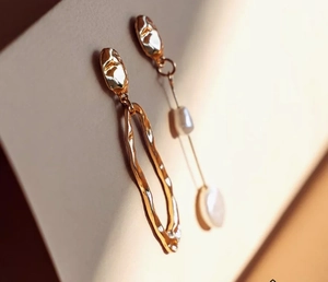 Macro shot of asymmetric gold earrings with hammered texture and baroque pearl pendants