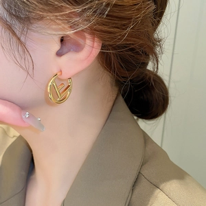 Close-up of golden geometric letter E stud earrings worn by a model in soft lighting