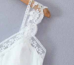 Close-up of white satin top featuring intricate floral lace trim and delicate embroidery