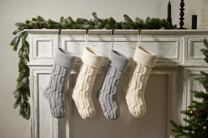 Close-up of four knitted Christmas stockings in grey and ivory hanging on a white fireplace
