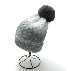 Detail of gradient knitted beanie with fluffy faux fur pompom and ribbed cuff