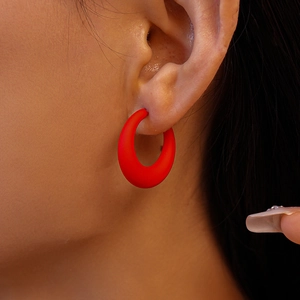 Close-up of a matte red circular acrylic hoop earring worn by a model