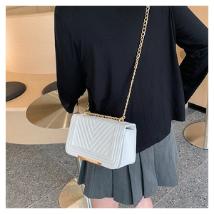 Close-up of white quilted crossbody bag with gold chain strap worn by a female model