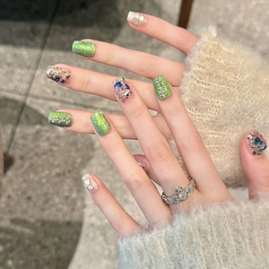 Close-up of cat-eye press-on nails with green glitter and purple crystal rhinestones