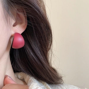 Close-up of matte red semi-sphere stud earrings worn by a model in a modern style