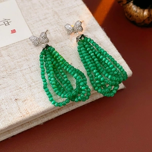 Close-up of green beaded tassel earrings with silver butterfly stud on vintage book