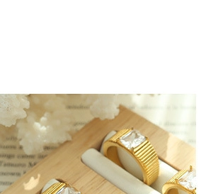 Detailed view of rectangular zircon gold ring with vertical ribbed band on wooden tray