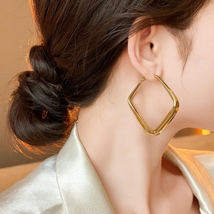 Modern minimalist large geometric square hoop earrings in golden metallic finish on model
