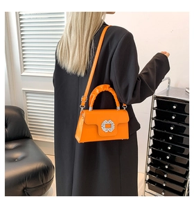 Bright orange crossbody bag with a rhinestone buckle shown in a stylish studio setting