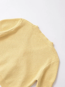Close-up of yellow knit top showing textured moss stitch fabric and ribbed crew neckline