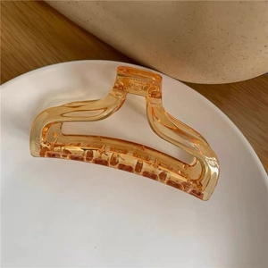Close-up of amber acrylic hair claw clip on white tray showing glossy resin texture
