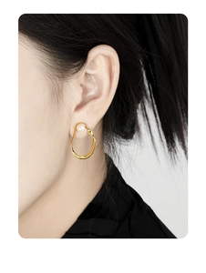 Detailed close-up of a hollow oval gold earring with an elegant inlaid white pearl
