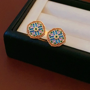Macro shot of gold-plated octagonal earrings with enamel flowers and green gemstones