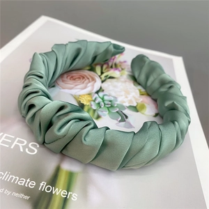 Detail shot of green pleated satin headband with silky texture on a magazine background
