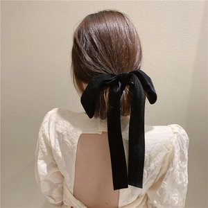 Detail of elegant black velvet hair bow with long ribbons on soft beige background