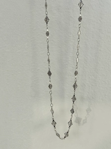 Macro view of silver geometric diamond plates on a long tassel belly chain necklace