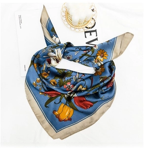 Detailed close-up of a blue floral silk scarf with tulip prints and gold-tone edges