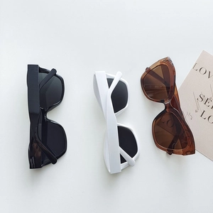 Detailed close-up of three cat-eye sunglasses in black, white, and brown on a flat gray background