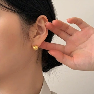 Close-up of golden wide hoop earrings with vertical ripple texture on female model