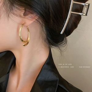 Golden double-hoop irregular twist C-shape earrings worn by a model in a side view