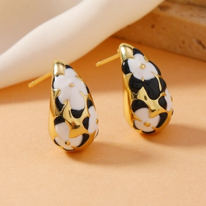 Macro shot of gold teardrop earrings featuring black and white enamel floral patterns
