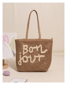 Detail of hand-woven straw tote bag featuring Bonjour embroidery and natural texture