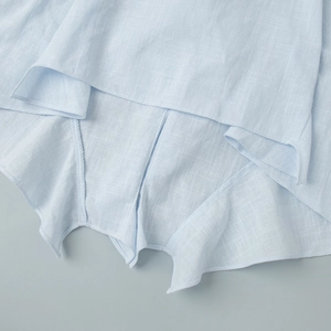 Macro detail of the ruffled hem and fine stitching on light blue cotton-linen fabric