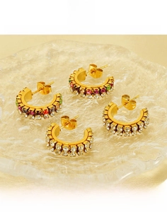 Close-up of gold titanium C-shaped earrings with colorful rhinestones on glass