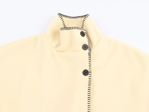 Detail of high neck wool coat with black contrast stitching and buttons on light yellow fabric