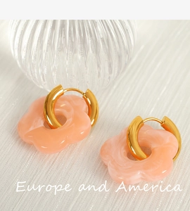 Macro shot of pink resin camellia flower earrings with golden hoops on white fabric