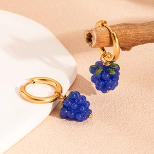 Créoles dorées avec pampilles de raisins bleus en résine et feuilles vertes sur texture