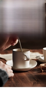 Close-up of retro Japanese ceramic coffee cup with saucer and steel spoon in warm light