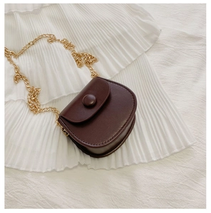Gros plan d'un sac selle en cuir PU marron foncé avec chaîne dorée sur tissu blanc