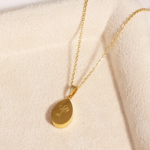 Détail du pendentif goutte dorée à motif floral en acier inoxydable sur tissu beige