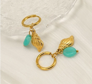 Dettaglio degli orecchini a cerchio dorati con ciondoli a conchiglia e pietre blu